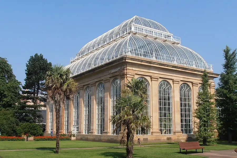 Glasshouse at the Royal Botanic Garden Edinburgh on a sunny day, with palm trees, lawn, and the historic greenhouse structure visible