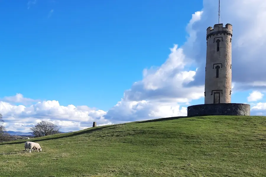 Binns Tower rising above the grassy hill at the House of the Binns, with sheep grazing below and blue sky overhead.