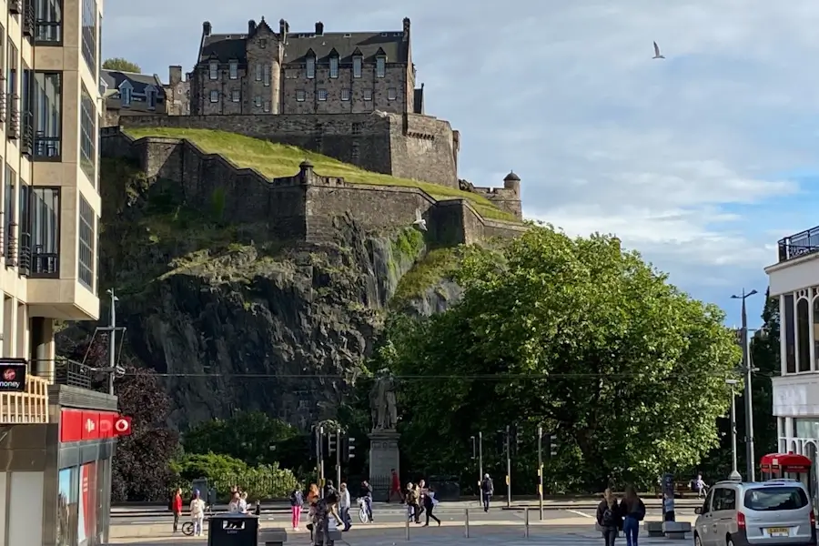 View from Castle Street looking toward Edinburgh Castle, with traffic, pedestrians, and trees lining the street in the city centre.