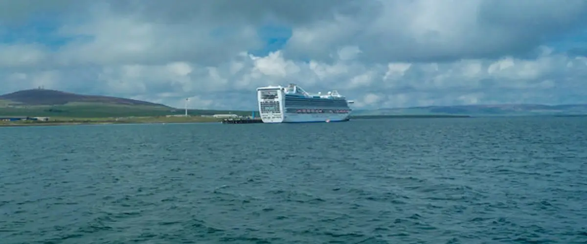 Cruise ship anchored off Kirkwall in Orkney with calm harbour waters and low shoreline in the distance