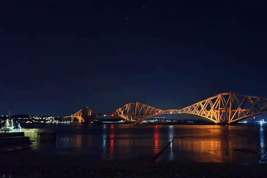 photograph forth bridge in queensferry at night with the illuminated harbour on the left and north queensferry in the background