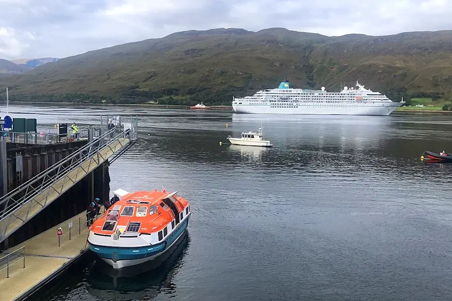 Cruise ship anchored in a Scottish port Fort William with tender boat operating near the pier and Highland coastline in the background