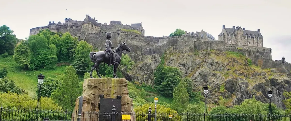 Edinburgh Castle rising above Castle Rock behind the Duke of Wellington statue in Princes Street Gardens