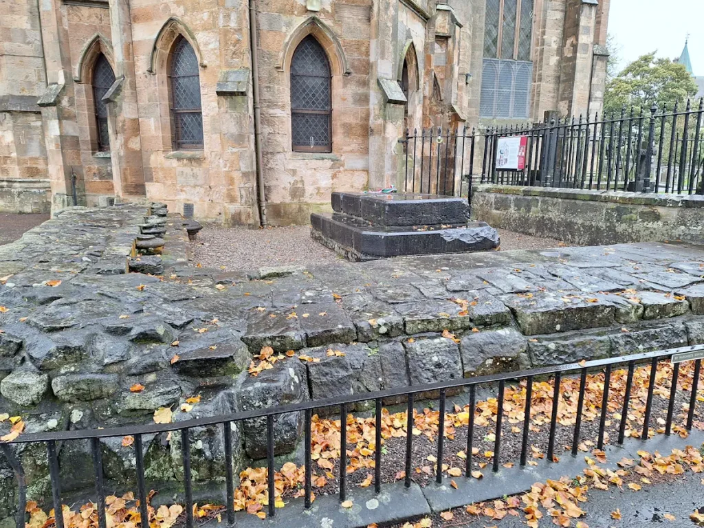 Remains of St Margaret’s shrine in the grounds of Dunfermline Abbey, railed off, with modern buildings behind